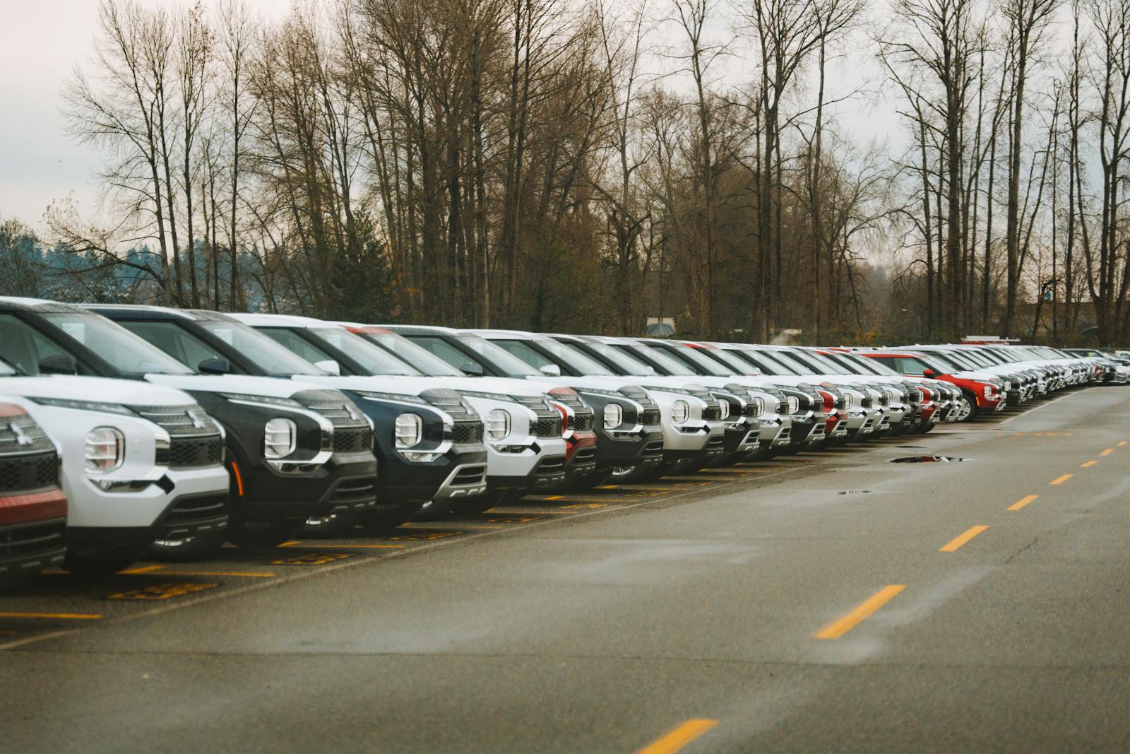 A line of brand new SUVs in an outdoor parking lot during a cloudy day.