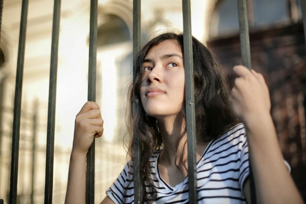 A teenage girl looks thoughtfully through bars, symbolizing hope and freedom.