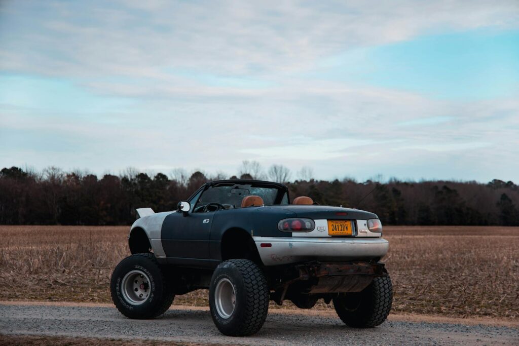 A unique customized convertible car with oversized tires parked in a rural landscape under a blue sky.