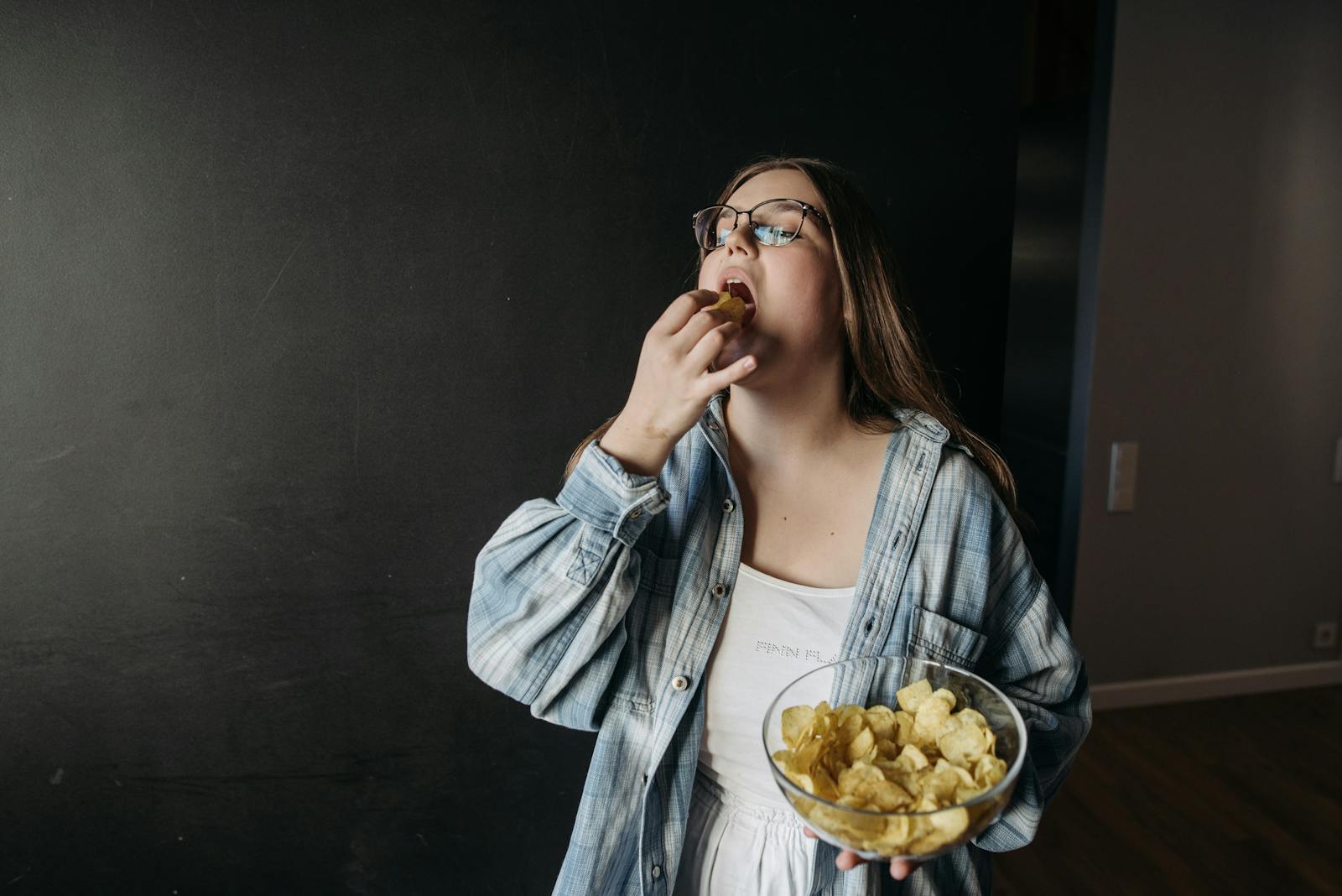 Young woman eating potato chips indoors, enjoying a snack moment.