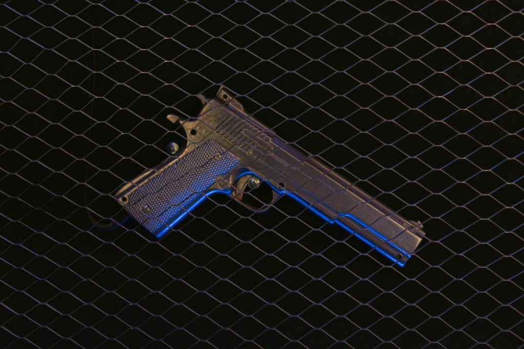 A pistol displayed behind wire mesh, illuminated by dramatic blue lighting.
